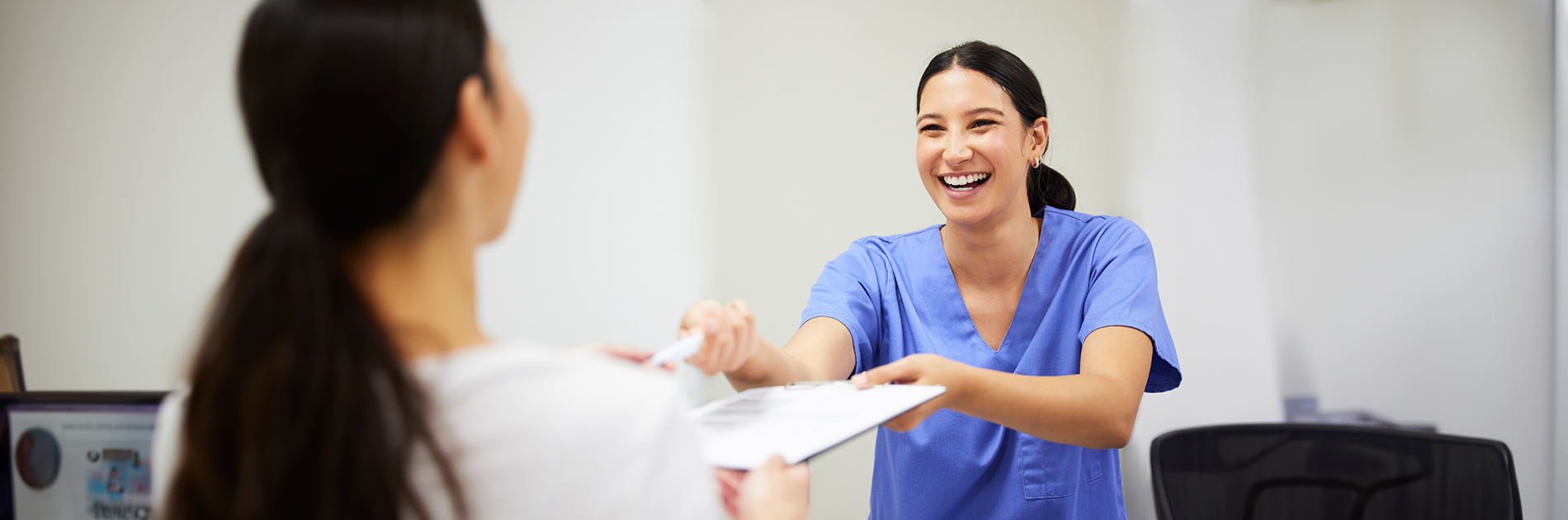 An adult woman in scrubs hands a card to another person who is seated and smiling at her.